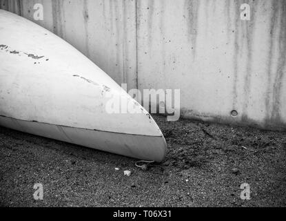 Kajak aus weißem Fiberglas Kunststoff mit im Alter von Marken mit weißen Kordel am Strand mit schwarzem Sand und Steine am Meer in der Nähe von Beton Wand ohne peo Stockfoto