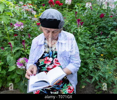 Ältere jüdische Frau das Tragen von Schmuck ihr Gebet buchen Sie im Garten im Hinterhof liest. Stockfoto