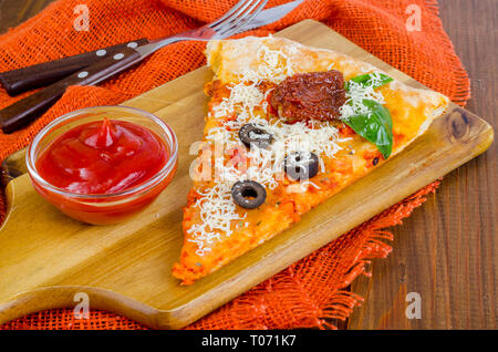 Stück Pizza mit getrockneten Tomaten, Oliven, Ketchup auf hölzernen Tisch. Studio Foto Stockfoto