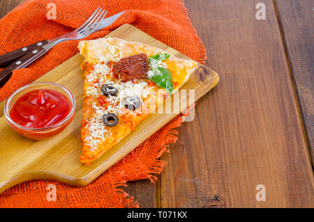 Stück Pizza mit getrockneten Tomaten, Oliven, Ketchup auf hölzernen Tisch. Studio Foto Stockfoto