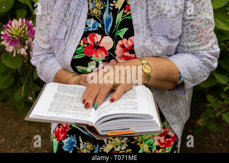 Ältere jüdische Frau das Tragen von Schmuck ihr Gebet buchen Sie im Garten im Hinterhof liest. Buch und Hände. Stockfoto