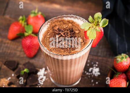 Erdbeere Schokolade Milchshake mit Schokolade Spänen, Kakao In großen Glas auf Holz- Hintergrund. Detailansicht, selektiver Fokus Stockfoto