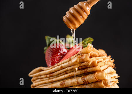 Honig goß Crepes oder Blini, schwarzer Hintergrund Detailansicht. Leckere süße Speisen Stockfoto