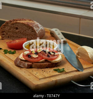 Roggen Sauerteig Brot mit Tomaten Oliven Mozzarella und rustikalen Board mit Messer Seitenansicht mit einigen natürlichen Licht Stockfoto