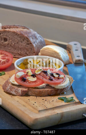 Roggen Sauerteig Brot mit Tomaten Oliven Mozzarella und rustikalen Board mit Messer Seitenansicht mit einigen natürlichen Licht Stockfoto