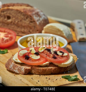 Roggen Sauerteig Brot mit Tomaten Oliven Mozzarella und rustikalen Board mit Messer Seitenansicht mit einigen natürlichen Licht Stockfoto