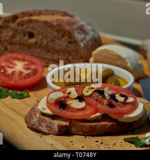 Roggen Sauerteig Brot mit Tomaten Oliven Mozzarella und rustikalen Board mit Messer Seitenansicht mit einigen natürlichen Licht Stockfoto