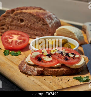 Roggen Sauerteig Brot mit Tomaten Oliven Mozzarella und rustikalen Board mit Messer Seitenansicht mit einigen natürlichen Licht Stockfoto