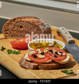 Roggen Sauerteig Brot mit Tomaten Oliven Mozzarella und rustikalen Board mit Messer Seitenansicht mit einigen natürlichen Licht Stockfoto