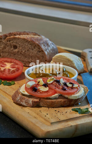 Roggen Sauerteig Brot mit Tomaten Oliven Mozzarella und rustikalen Board mit Messer Seitenansicht mit einigen natürlichen Licht Stockfoto