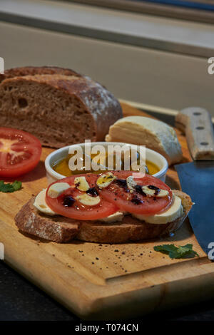 Roggen Sauerteig Brot mit Tomaten Oliven Mozzarella und rustikalen Board mit Messer Seitenansicht mit einigen natürlichen Licht Stockfoto