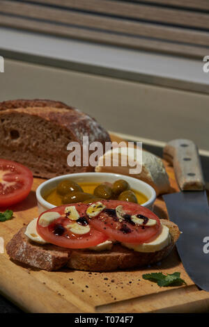 Roggen Sauerteig Brot mit Tomaten Oliven Mozzarella und rustikalen Board mit Messer Seitenansicht mit einigen natürlichen Licht Stockfoto