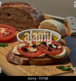 Roggen Sauerteig Brot mit Tomaten Oliven Mozzarella und rustikalen Board mit Messer Seitenansicht mit einigen natürlichen Licht Stockfoto