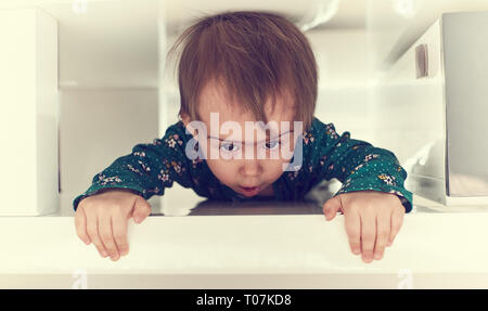 Cute kaukasische Baby girl Kriechen durch engen Raum unter dem Tisch in Richtung Kamera. Garbing Kante des Tisches und puling ihr Selbst heraus. Kopieren Sie Speicherplatz auf righ Stockfoto