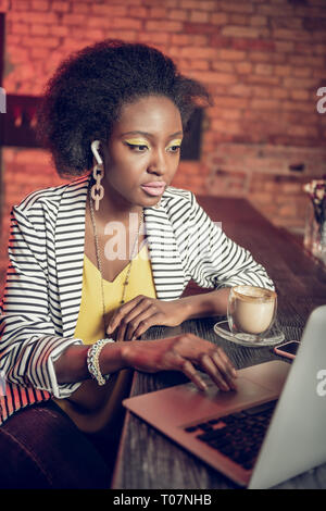 Ernsthafte Afro-amerikanische 20-jähriges Mädchen Arbeiten am Laptop in der Bar Counter Stockfoto