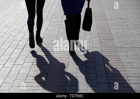 Zwei Frauen auf der Straße, schwarze Silhouetten und Schatten auf Pflaster. Schlanke Beine in Stiefeln, Konzept der weiblichen Mode, Freundschaft, dramatische Leben Stockfoto