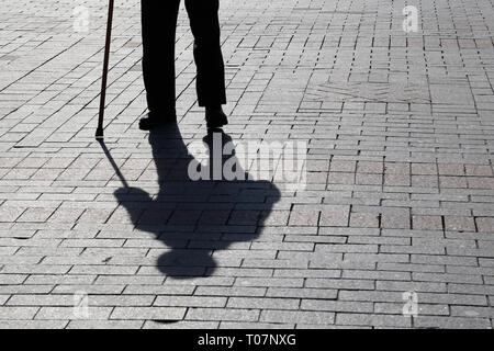 Silhouette der Mann mit einem Stock, lange Schatten auf Pflaster. Konzept der hinkt oder blind Person, Invalidität, Alter, Armut, Krankheiten der Wirbelsäule Stockfoto