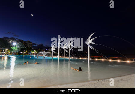 Menschen schwimmen in der beleuchteten Lagune mit Fischen Skulpturen auf Cairns Esplanade am Abend, Far North Queensland, FNQ, QLD, Australien Stockfoto