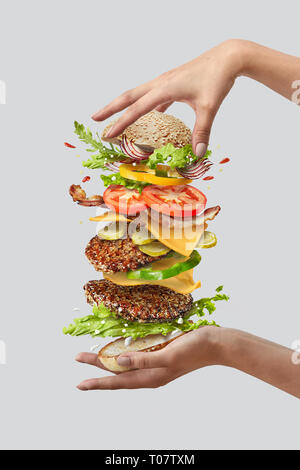 Girl's Händen halten große leckere hausgemachte Burger mit fliegenden natutal Zutaten auf einem weißen Hintergrund. Kopieren Sie Platz. Stockfoto