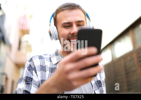 Glückliche Menschen mit Kopfhörern Musik hören prüfen Smart Phone zu Fuß auf der Straße Stockfoto