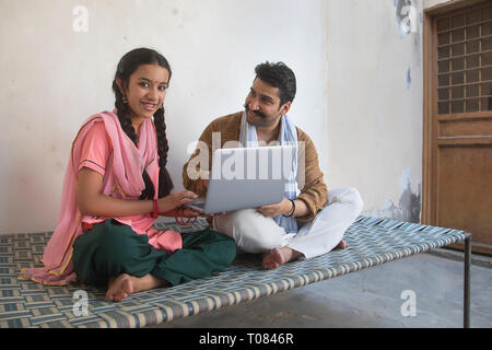 Happy Village Mädchen sitzen mit ihrem Vater auf einem Feldbett mit Laptop Computer. Stockfoto