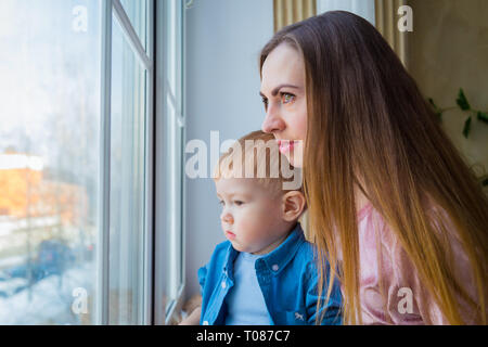 Junge Mutter und nachdenkliche kleine Junge Blick durch Fenster Stockfoto