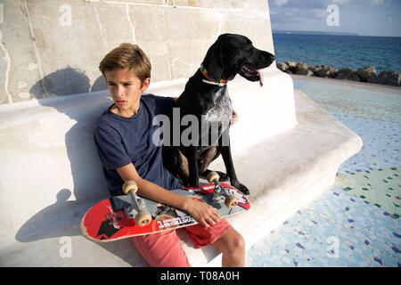 Junge mit Skateboard und Hund am Strand Stockfoto