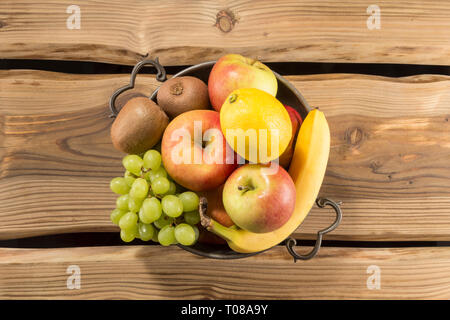 Köstliche frische Früchte in einer Schale auf rustikale Holzplanken Oberfläche: Kiwis, Zitrone, Apfel, Banane, Weintrauben. Stockfoto