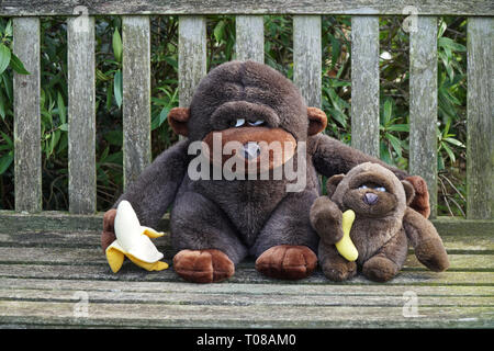 Die großen und kleinen Gorillas, die auf einer Bank sitzen und entspannen beim essen Bananen Stockfoto