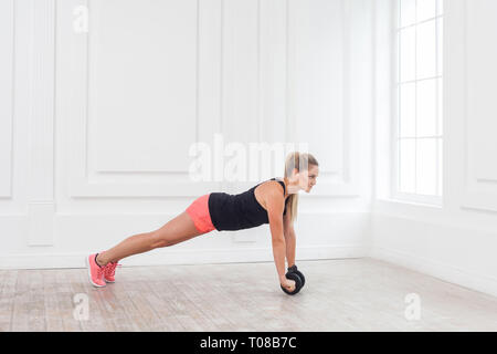 Volle Länge Seitenansicht Portrait von athletischen jungen Frau in fit mit Hanteln in den Fitnessraum zu trainieren und auf perfekte Plank. Innen-, Studio shot Stockfoto