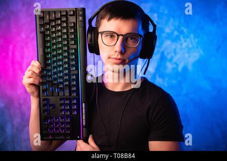 Technologie, Cyberspace, Programmierung und Personen Konzept - Hacker Mann in Headset und Brillen mit Tastatur über Neon Wand Stockfoto