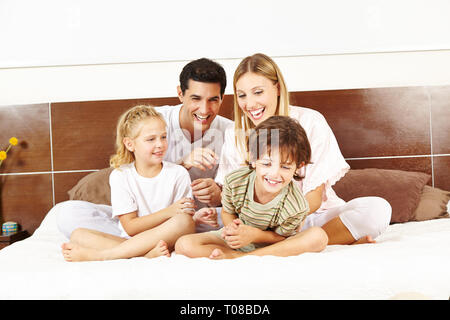 Lachend Familie sitzt im Bett mit zwei Kindern und Kitzeln einander Stockfoto