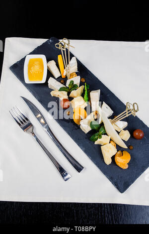 Käseplatte Sortiment von verschiedenen Arten von Käse auf dunklem Schiefer Schneidebrett. Camembert, Rokoko, Parmesan, Nüsse, Tomaten, Mandarin, o Stockfoto