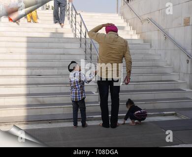 NEU-DELHI, INDIEN – 2018. MÄRZ: Ein Mann und zwei Kinder waschen sich die Füße, bevor sie Gurdwara Bangla Sahib am Connaught Place, Neu-Delhi, hinaufgehen. Stockfoto