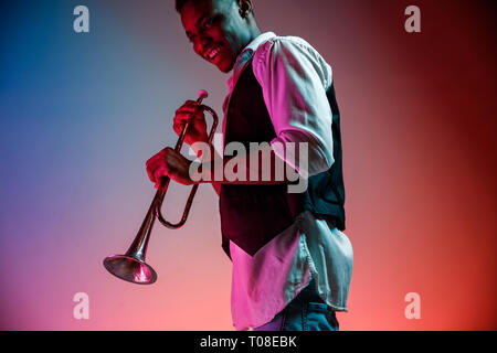 African American stattlichen Jazz Musiker spielen Trompete in der Studio auf einem neon Hintergrund. Musik Konzept. Junge freudige attraktiver Kerl improvisieren. Close-up retro Portrait. Stockfoto