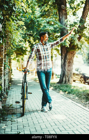 Ein hübscher junger Mann geht in die Stadt fahren mit dem Fahrrad, daneben stehen und winken. Stockfoto