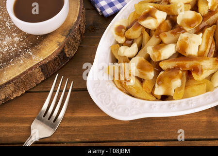 Poutine Platte auf einem hölzernen Hintergrund. Mit Pommes frites, Soße und Quark zubereitet. Kanadische Küche. Stockfoto