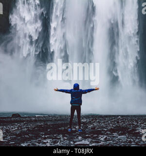 Eine Person admirnig die Schönheit der Skogafoss Wasserfall in Island entfernt Stockfoto