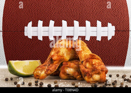 Chicken Wings mit Limetten Keil, Salz und Pfeffer auf konkrete Tabelle. Fußball-ball Bild im Hintergrund. Stockfoto