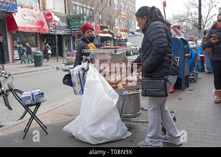 An einem kalten Wintertag, zwei Frauen Verkauf von frisch gegrilltem Mais & gegrilltem Fleisch. Auf der 82nd St. in Jackson Heights, Queens, New York City in der Nähe des erhöhten #7 Zug. Stockfoto