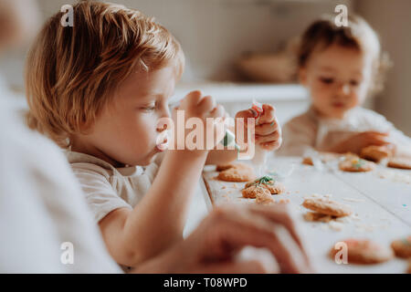 Zwei kleine kleinkind Kinder am Tisch sitzen, Dekorieren und essen Kuchen zu Hause. Stockfoto