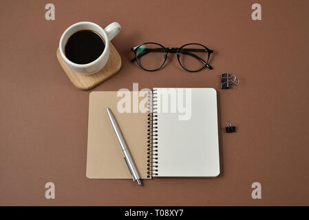 Mockup Arbeitsbereich mit Büromaterial, Stift, Kaffeetasse, Notepad und Gläser auf braunem Hintergrund. Flach, Ansicht von oben, kopieren Raum Stockfoto