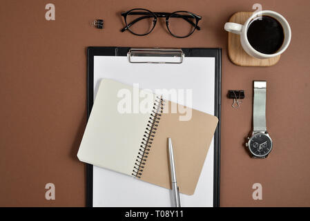 Ansicht von oben Bürotisch Schreibtisch. Mit leeren Clip Board, Uhr, Bürobedarf, Pen und Brillen auf braunem Hintergrund Arbeitsbereich. Flach, kopieren Raum Stockfoto