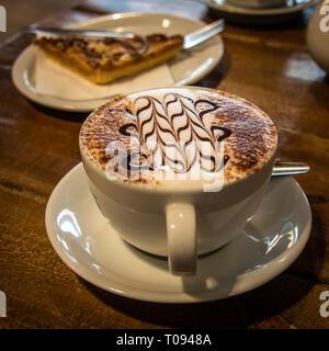 Eine heiße Tasse Cappuccino und Kuchen auf einem Holztisch Stockfoto