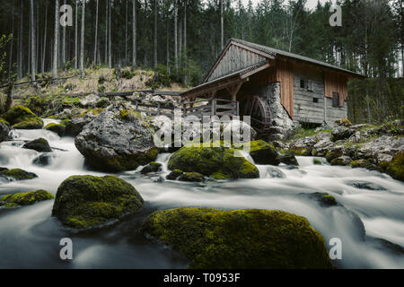 Idyllische lange Belichtung Blick auf eine alte verlassene Mühle mit bemoosten Felsen im wunderschönen Flussbett in einem mystischen Wald liegt an einem bewölkten Tag im Springtim Moody Stockfoto