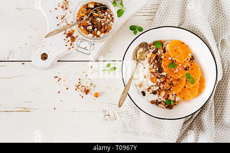 Schüssel mit hausgemachtem Müsli mit Joghurt und Tangerine auf weissem Holztisch. Fitness Nahrung. Ansicht von oben Stockfoto