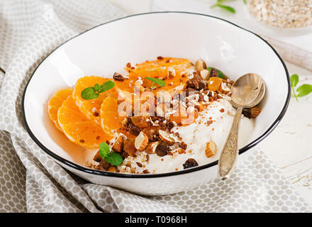 Schüssel mit hausgemachtem Müsli mit Joghurt und Tangerine auf weissem Holztisch. Fitness Nahrung. Stockfoto
