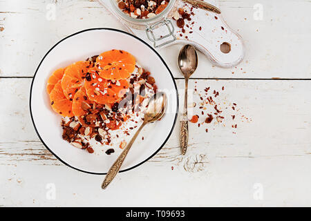 Schüssel mit hausgemachtem Müsli mit Joghurt und Tangerine auf weissem Holztisch. Fitness Nahrung. Ansicht von oben Stockfoto