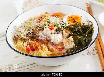 Miso Ramen asiatische Nudeln mit Kohl Kimchi, Algen, Eier, Pilze und Käse Tofu in Schüssel auf weiße Holztisch. Koreanische Küche. Stockfoto