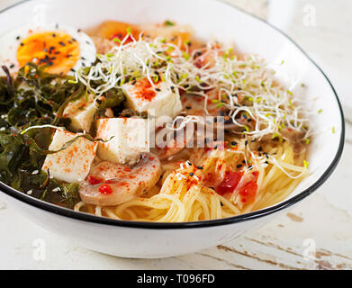 Miso Ramen asiatische Nudeln mit Kohl Kimchi, Algen, Eier, Pilze und Käse Tofu in Schüssel auf weiße Holztisch. Koreanische Küche. Stockfoto